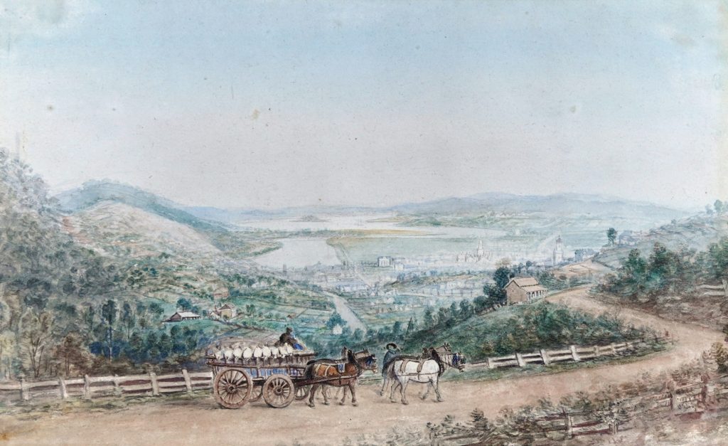 Watercolour. View of town set between hills, with water inlet from sea visible. In the foreground a cart drawn by four horses on a dirt track road.